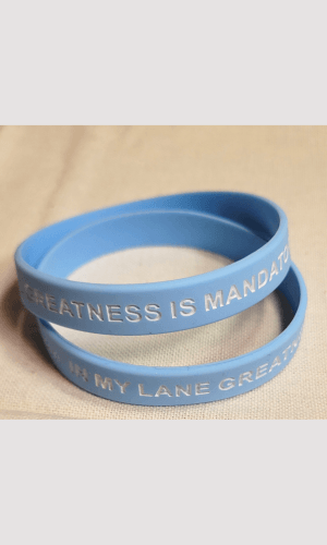 Blue affirmation bracelet with "Greatness Is Mandatory" phrase, representing personal empowerment.